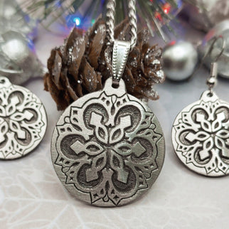 Snowflake pendant and earrings from Atlantic Pewter with a pine cone and lights on the background