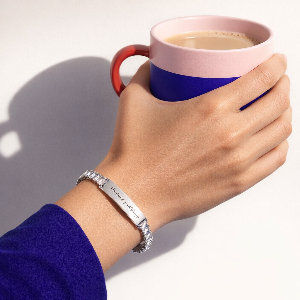 Hand holding a pink and blue mug with a silver bracelet on a white background