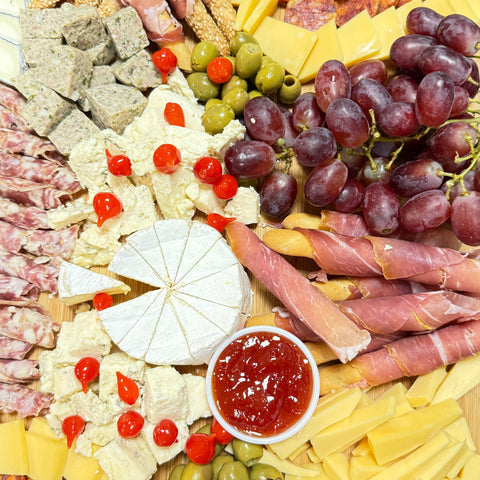 Assorted meats, cheeses, and fruits on a platter with a small bowl of red sauce.
