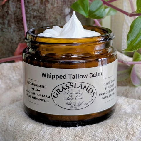 Jar of Grasslands Whipped Tallow Balm with a white label on a textured surface with plants in the background.