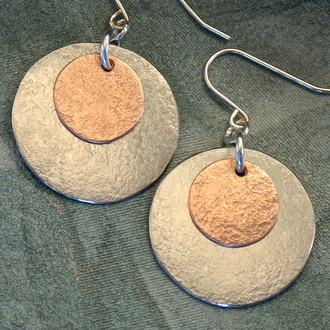 a pair of earrings with a copper and silver disc