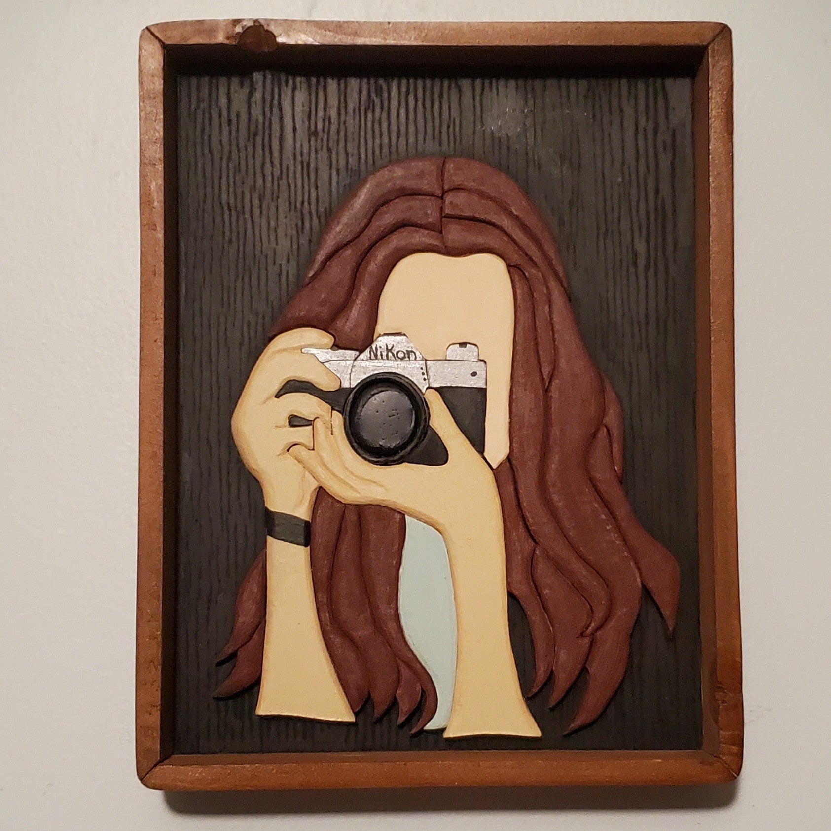 Wooden frame with a cutout of a woman holding a camera, on a plain background